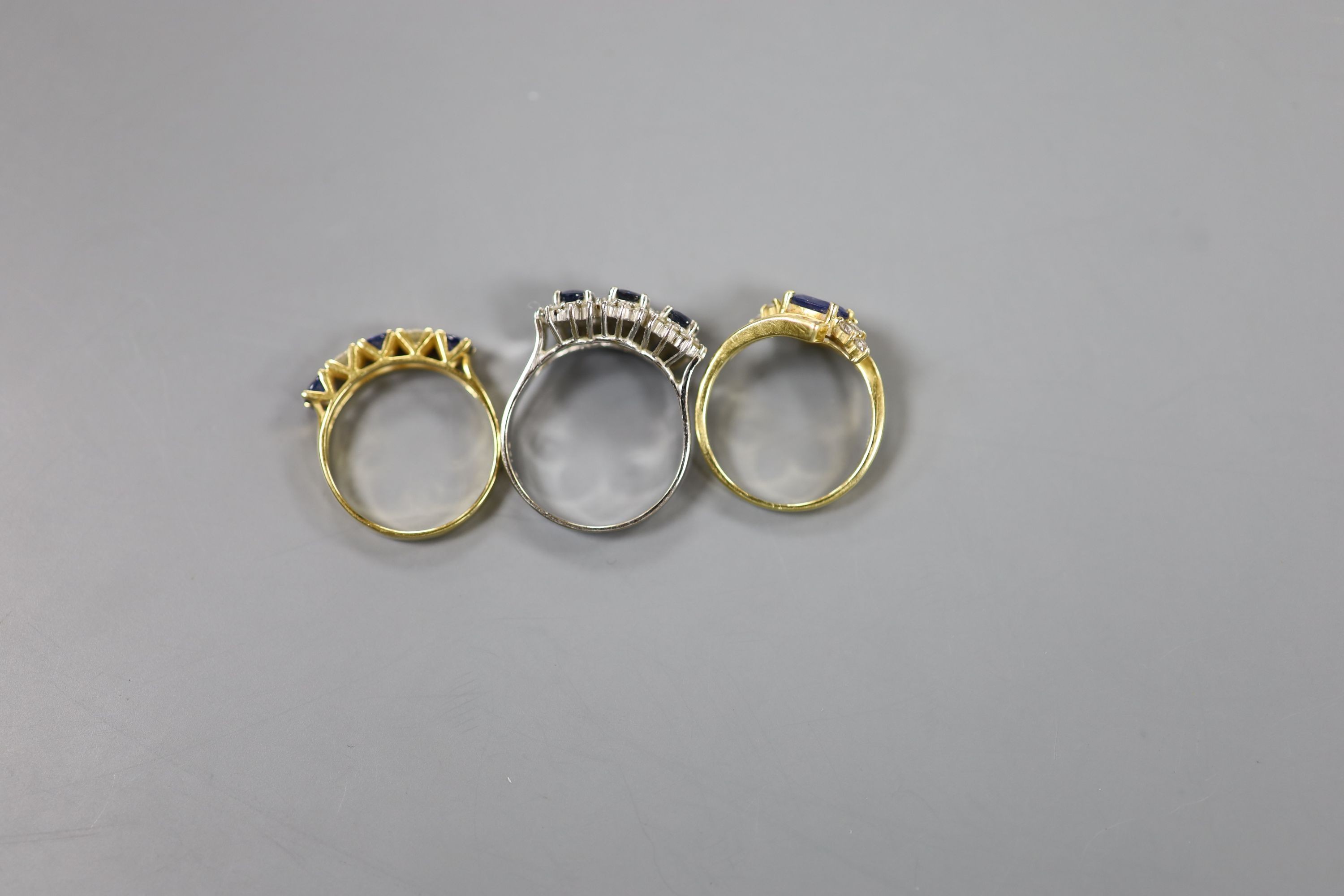 A modern 7560 white metal, sapphire and diamond set triple cluster ring, size Q/R and two other 18k, sapphire and diamond set dress rings, including half hoop, sizes O & N, gross weight 13.1 grams.